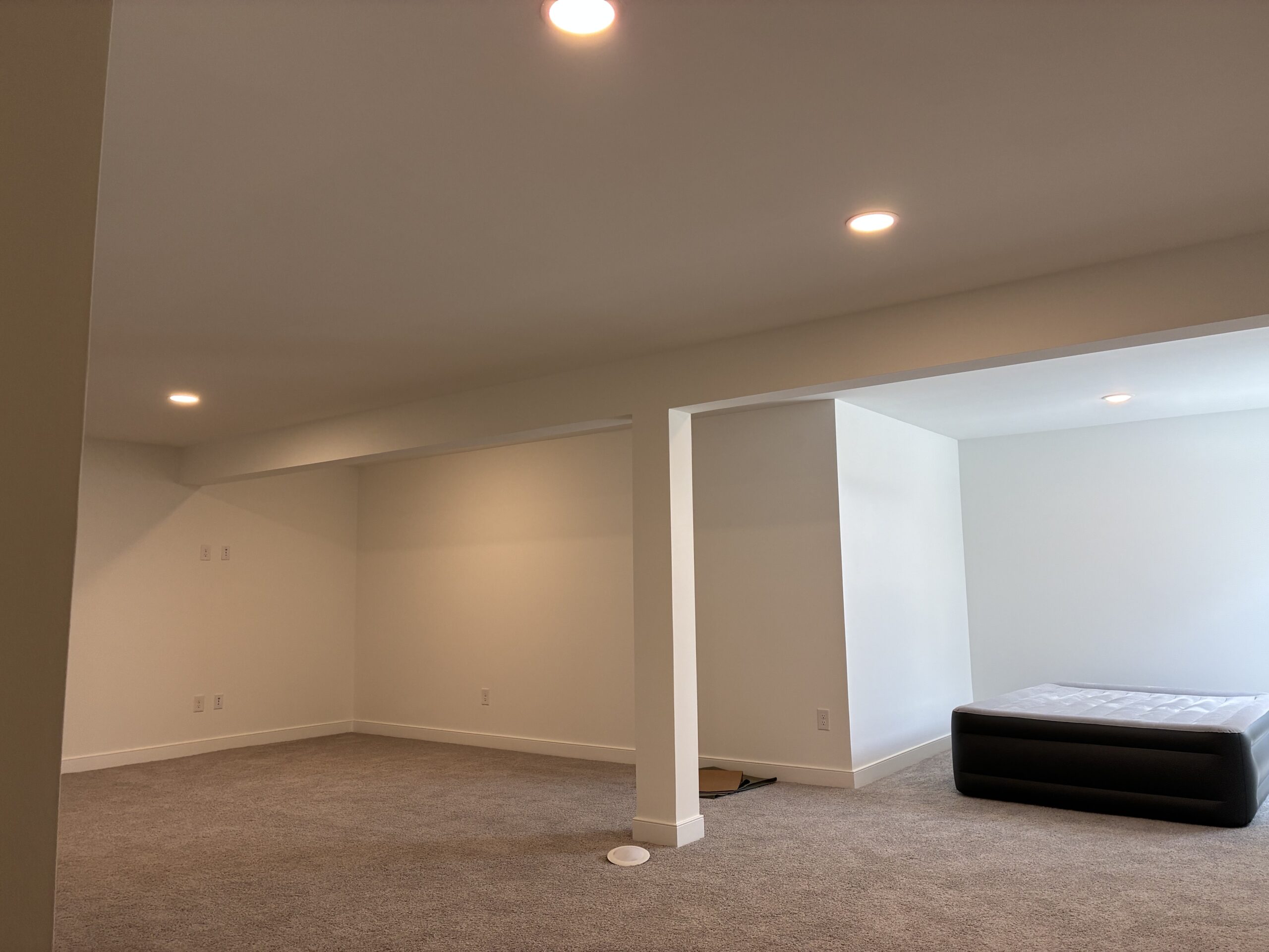 Spacious, empty basement area with carpet, recessed lighting, and an unmade air mattress in the corner.