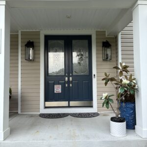 Elegant front porch featuring double glass doors, decorative lanterns, and potted plants on a stone-accented entryway.